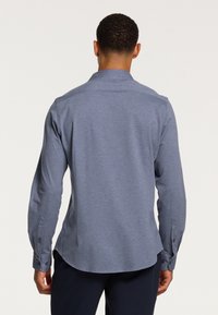 Srajca z dolgimi rokavi in ovratnikom iz svetlo modrega bombažnega zmesi. Ima ravno hrbtno stran, gumbaste manšete in gladko teksturo.