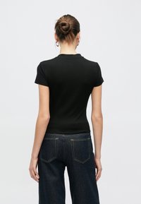 T-shirt nero in cotone a maniche corte con design aderente. Paio di jeans in denim scuro con cuciture gialle e stile a cinque tasche.