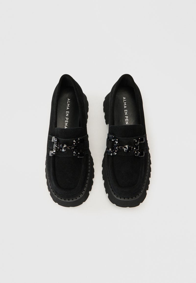 Czarne zamszowe mokasyny z masywną, teksturowaną podeszwą. Ozdobne czarne elementy metalowe ozdabiają cholewkę. Minimalistyczny design z prostymi liniami.