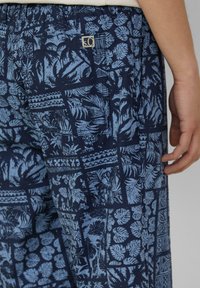 Marineblauwe shorts met een tropisch print in lichtblauw, met een rasterindeling, een elastische tailleband en een klein logo detail aan de achterkant.