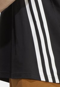 T-shirt nera con tre strisce verticali bianche sul lato sinistro. Il tessuto appare liscio con un classico collo a giro.