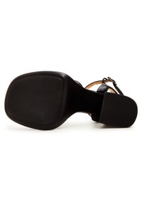 Sandal con tacco nero caratterizzato da una suola texture, una cinghia alla caviglia e una parte superiore liscia. Il design enfatizza un'estetica minimalista.