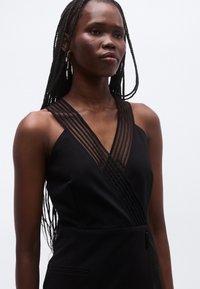 Mustast ilma varrukateta kleidist, mis on ristatud disainiga, millel on kaelaosas läbipaistev horisontaalne paneel ja sile tekstuur.