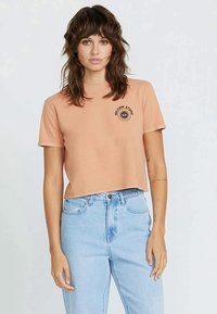 Light peach cropped t-shirt made of cotton, featuring a round neckline and short sleeves, with a black sun logo on the left chest area.
