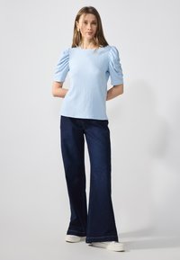 Ljust blått texturerat plagg med puffärmar, kombinerat med mörkblå vida jeans och vita sneakers. En enkel, avslappnad outfit.