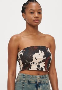 Top crop bandeau dintr-un material smântânos cu un imprimeu abstract de vacă în nuanțe de maro și negru. Design ajustat, textură netedă și fără accesorii vizibile.