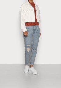 Valkoinen cropped-farkkutakki, ruosteenvärinen kuosillinen neulepaita, vaaleansiniset kulutetut farkut repeämillä ja valkoiset korolliset lenkkarit.