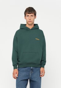 Felpa verde con cappuccio e tasca a marsupio, con un logo arancione sul lato sinistro del petto. Realizzata in un morbido tessuto misto cotone dalla texture piacevole.