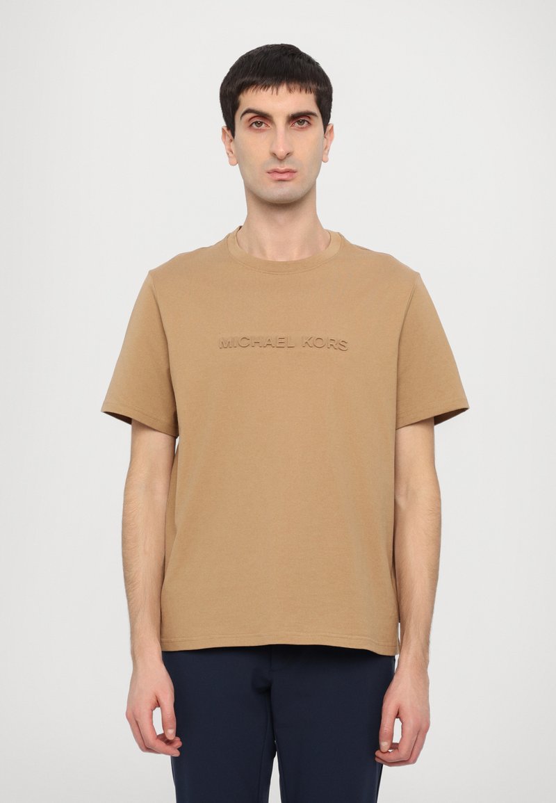 Brown cotton t-shirt with short sleeves and a crew neckline; features embossed text "MICHAEL KORS" on the front. Designed for a relaxed fit.