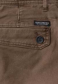 Brun mönstrad tyg med en bakficka som har en svart knapp och en liten etikett som säger "STREET ONE MEN Unmatched Comfort."