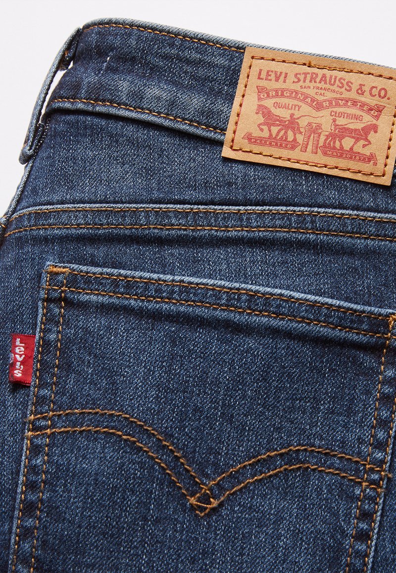 Jean en denim bleu foncé avec une patch en cuir à la taille, ornés de coutures orange et d'une petite étiquette rouge avec "Levi's" sur la poche arrière.