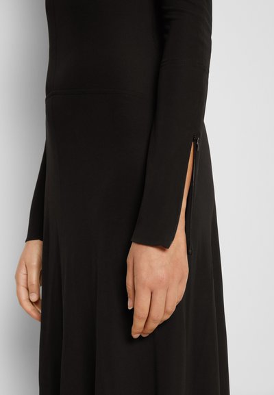 Vestido preto de manga longa feito de um material suave, com um fecho lateral na parte inferior e uma barra rodada.