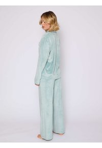 Conjunto de loungewear en verde menta hecho de una tela suave y esponjosa. Presenta mangas largas y pantalones de piernas anchas, con un corte relajado y una textura suave.
