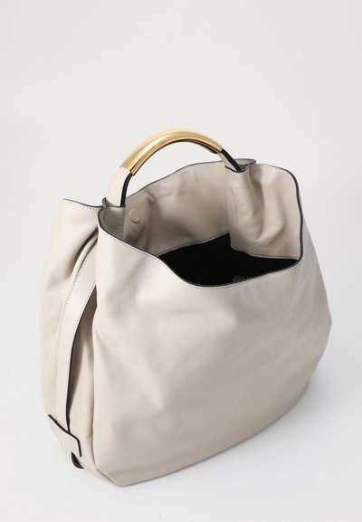Beige leather hobo bag with a curved gold handle, soft texture, and black interior lining; features a minimalist design and open top.