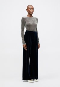 Un haut long à manches en velours gris associé à un pantalon large en velours bleu marine. Des talons aiguille blancs viennent compléter la tenue.