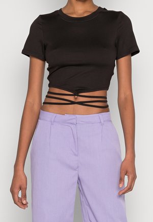 Sort cropped t-shirt med korte ærmer og et knyttet design, parret med lyse lavendelfarvede bukser med høj talje og plisserede frontlommer.
