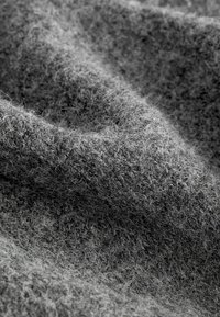 Gros plan sur un tissu en laine gris épais et texturé avec des fibres visibles et des plis doux.