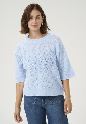 Jasnoniebieski sweter z dzianiny w wzór zygzakowy, krótki rękaw i ściągacz przy dekolcie, zestawiony z dżinsami. Miękka, strukturalna tkanina.