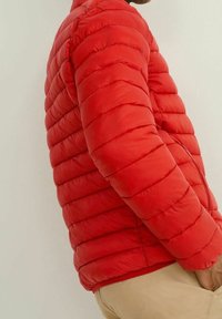 Veste matelassée rouge avec sections horizontales, dotée d'une fermeture éclair frontale, de matériaux légers et d'une coupe ajustée.