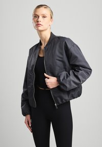 Black bomber jacket with a zip front, ribbed collar and cuffs, and elastic waistband. Smooth fabric with a slightly shiny texture.