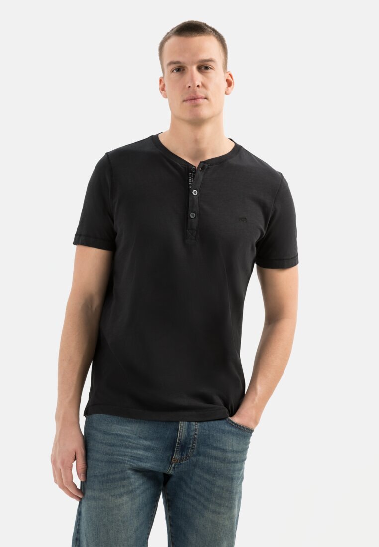 Schwarzes kurzärmliges Henley-Shirt mit rundem Halsausschnitt, drei Knöpfen und einem dezenten Logo auf der Brust; kombiniert mit blauen Jeans.