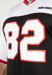 Jersey negro con mangas blancas, con acentos rojos llamativos y grandes números blancos "82". El texto dice "EQUIPO GORILA" cerca del collar.