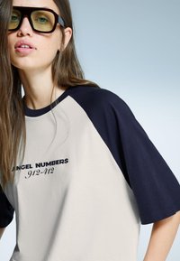 Kremna in mornarsko modra oversized majica s kratkimi raglan rokavi, na sprednji strani je v črni barvi natisnjen napis "ANGEL NUMBERS 912-412". Gladka tekstura.