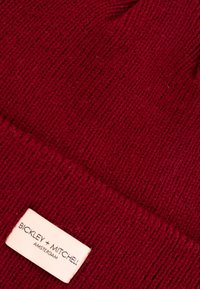 Bordeaux gebreide beanie met ribbeltextuur en genaaide label; label zegt "BICKLEY + MITCHELL, AMSTERDAM."