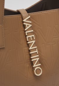 Kabelka z tanového kůže s vyraženým logem, plochým popruhem se zlatým kováním zobrazujícím slovo "VALENTINO."