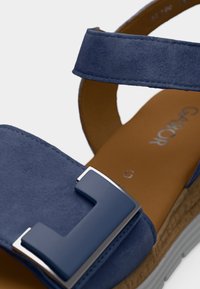 Μπλε σουέντ σανδάλι με ρυθμιζόμενο λουράκι, ταμπά επενδυμένο πέλμα, και διακοσμητική σκούρα μπλε αγκράφα σε υφή σόλας.
