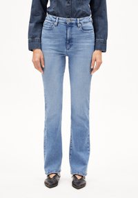 Hellblaue Jeans mit hoher Taille, geradem Bein und klassischem Fünf-Taschen-Design, kombiniert mit schwarzen Ballerinas. Glatte Textur.