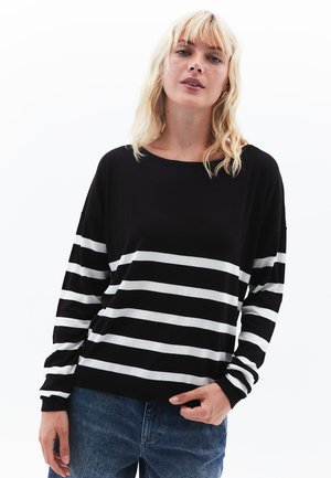 Mustavalkoinen raidallinen neule, jossa on pitkät hihat, pyöreä pääntie ja ribbireunus; yhdistettynä vaaleansinihin farkkuihin.