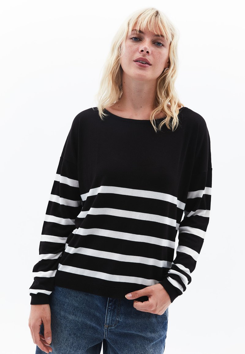 Schwarz-weißer gestreifter Pullover mit langen Ärmeln, rundem Ausschnitt und geripptem Saum; kombiniert mit hellblauen Jeans.