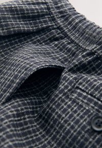 Marineblauwe gestructureerde stof met een rasterpatroon, voorzien van een elastische tailleband en knoopdetail. Close-up van het ingewikkelde weefsel en ontwerp.