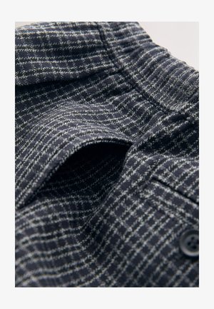 Marineblauwe gestructureerde stof met een rasterpatroon, voorzien van een elastische tailleband en knoopdetail. Close-up van het ingewikkelde weefsel en ontwerp.