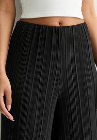 Zwarte plissé brede broek met hoge tailleband, voorzien van verticale plooien voor textuur en een soepele afwerking van lichtgewicht stof.