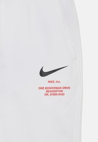 White Nike sweatpants featuring a black swoosh logo and red text with the brand's name and address on the right side. Smooth texture.