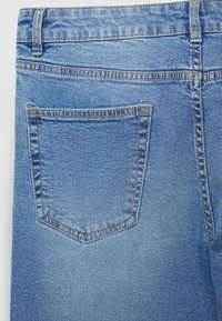 Jeans aus hellblauem Denim mit einer einzelnen Gesäßtasche, die geschwungene Nähte aufweist, und einer leicht ausgewaschenen Textur.