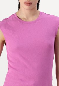Rosa, ribbet skjorte uten ermer med rund halslinning. Teksturen er glatt og tettsittende, uten synlige mønstre eller pynt.