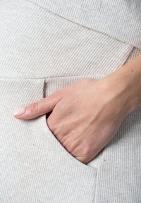 Hellbeige gerippter Stoff mit einer Tasche, in der eine Hand teilweise steckt. Die Textur wirkt weich und flexibel, mit subtilen Variationen.