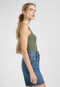 Top in cotone ribattuto verde oliva con spalline sottili abbinato a una gonna in denim blu alta in vita. La texture è liscia; la gonna presenta tasche classiche.