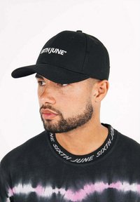 Cappellino nero da baseball con logo ricamato "SIXTH JUNE". Il cappello presenta una visiera curva e un design aderente. La cucitura assiale è visibile.