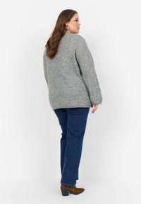 Maglione grigio a maglia con vestibilità ampia e spalle cadenti, abbinato a jeans in denim blu e stivaletti con tacco marroni. Design semplice.