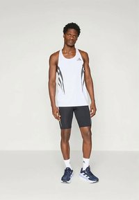 Biely športový top bez rukávov s čiernymi prúžkami, kombinovaný s čiernymi šortkami. Doplnky zahŕňajú námornícke topánky a biele ponožky. Voľný športový outfit.