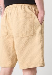 Light beige shorts with a textured, ribbed design, featuring side pockets and an elastic waistband.