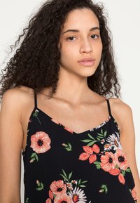 Camisola floral preta com decote em V, alças finas e uma mistura de flores rosa e brancas com folhas verdes, feita de tecido leve.