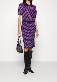 Vestito lavorato a maglia con motivo geometrico viola, nero e rosa, abbinato a stivali neri al ginocchio e una piccola borsa nera.