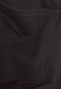 Černá bavlněná tkanina s hladkým texturem, s malou přední kapsou a viditelnými švy, což vytváří jednoduchý design.