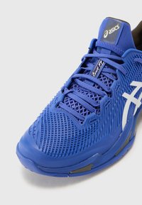 Blauer Sportschuh mit einem Mesh-Obermaterial, strukturierten Oberflächen, flachen Schnürsenkeln und einem weißen Logo. Verfügt über eine gepolsterte Sohle und eine verstärkte Zehenkappe.