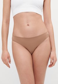 Chiloți bikini bej fără cusături, cu un design minimal și o textura netedă, având un tiv jos și fără cusături vizibile.